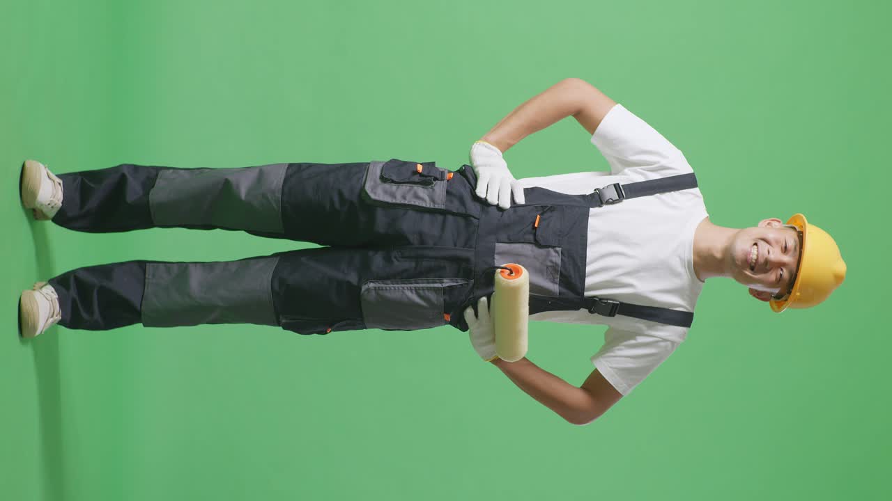 Full Body Of Asian Man Painter Wearing Safety Helmet Standing With Arms Akimbo Looking At Camera And Smiling In The Green Screen Background Studio