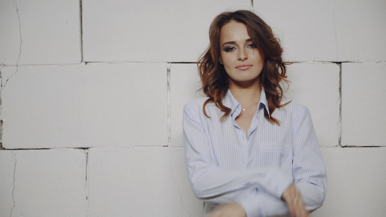 Woman in a light blue shirt against a white brick wall