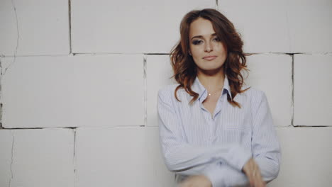 woman in a light blue shirt against a white brick wall