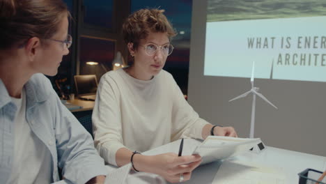 young female engineer holding paper slides and presenting sustainable energy startup to business team during office meeting in the evening