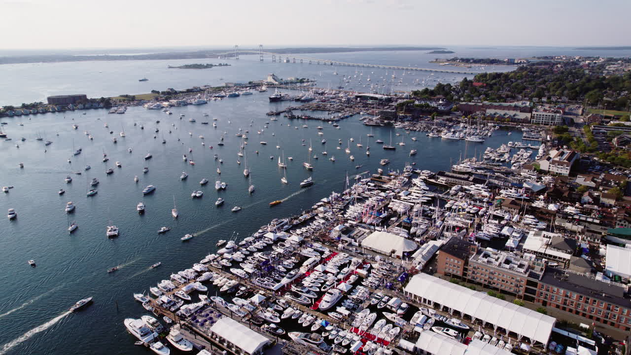 A drone shot of Newport, Rhode Island, USA, flying over the harbor away from the bridge, showcasing numerous sailboats and yachts below. Ideal for maritime, coastal, and travel projects.