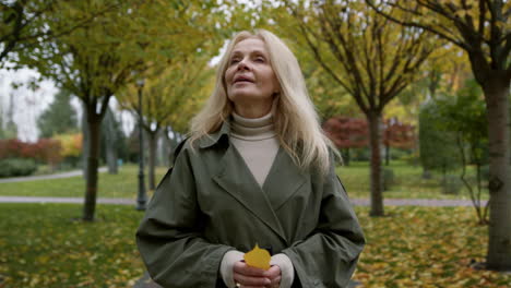 Portrait-of-beautiful-woman-walking-in-autumn-park.-Elderly-lady-holding-leaves