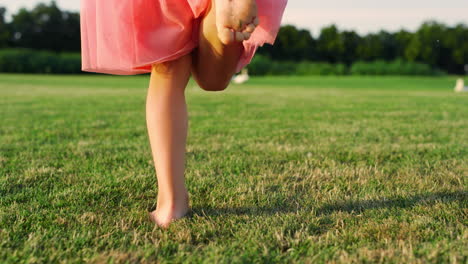 rear view of unrecognizable girl running barefoot on green grass at city park.