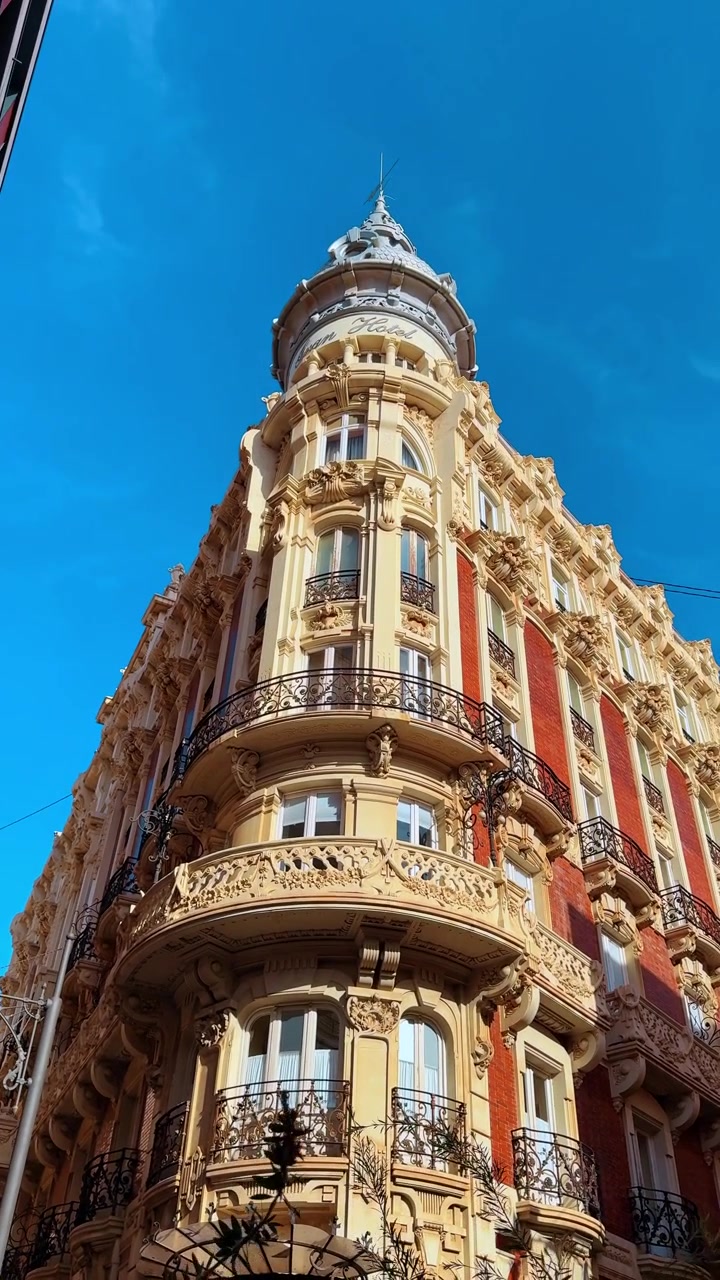 Vista dal basso di un edificio storico ornato ad Alicante. Dettaglio architettonico di un edificio storico giallo e rosso con balconi e una torretta contro un cielo blu chiaro