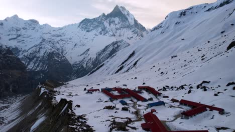 Aerial-View-Of-Annapurna-Base-Camp-On-Snow-Covered-Mountain-Side-With-Machapuchare-Peak-In-Background