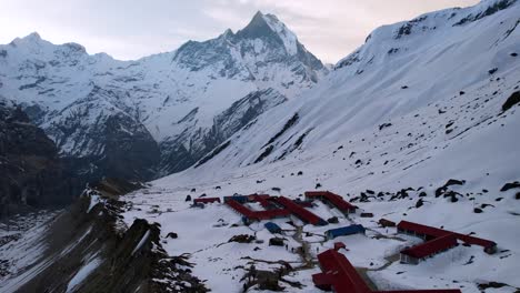 aerial view of annapurna base camp on snow covered mountain side with machapuchare peak in background