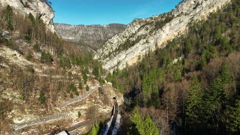 cars driving over the road in the jura gorges at moutier in switzerland on a cold sunny autumn day with snow on the mountains in the background