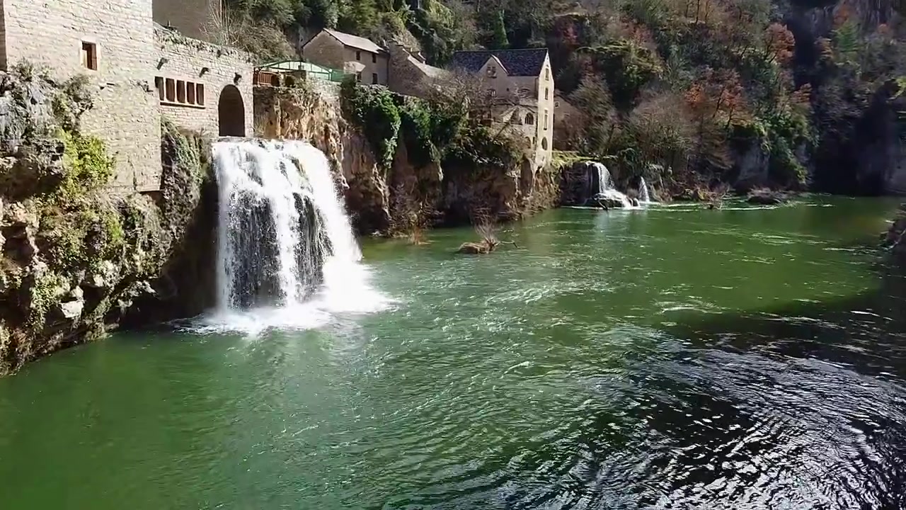 Cascata di Saint-Chély-Du-Tarn. Gole del Tarn. Cascata. Cascata accanto a case in pietra lungo il fiume. Vista aerea ravvicinata. Francia.