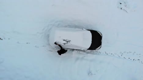 El-Hombre-Barre-La-Capa-De-Nieve-Congelada-Del-Auto-Negro-Después-De-La-Nevada-Invernal,-Antena