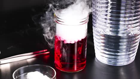 a vibrant chemical reaction produces fuming smoke from a red liquid in a glass jar, creating a dynamic visual effect