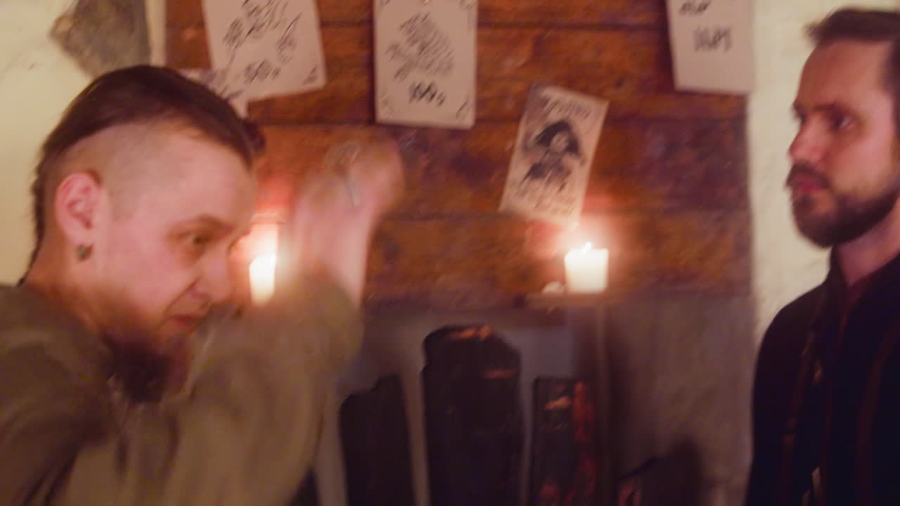 남자 손님은 술집에서 춤을 추고 게시판을 알아차립니다. 술에 취한 레인저는 재미를 멈추고 중세 술집의 발표를보고 있습니다. 판타지 게임 캐릭터. 손 카메라.