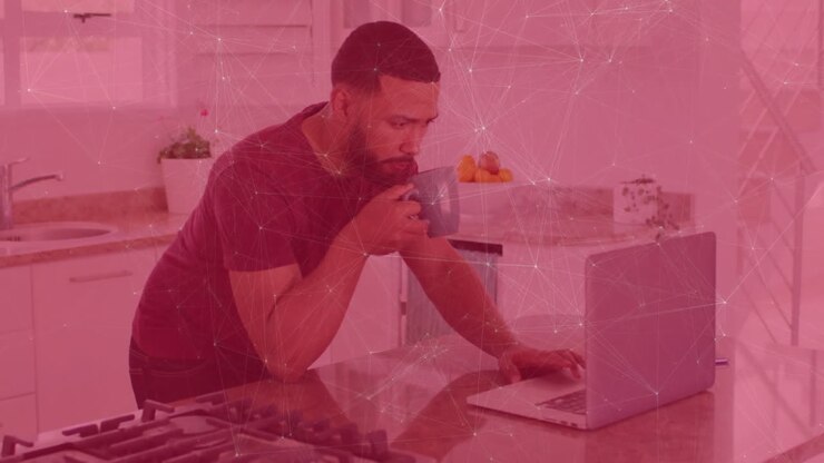 man sipping coffee from mug on kitchen island while viewing animated finance charts on laptop