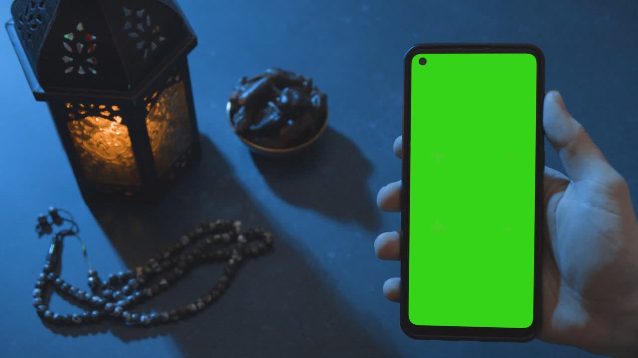 toma amplia de agua de linterna y dátiles con un teléfono de pantalla verde al atardecer