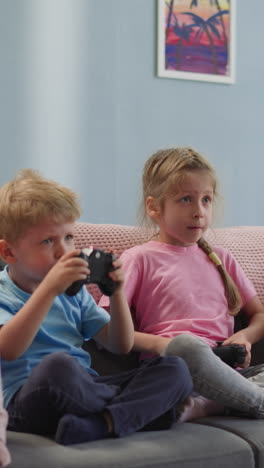 toddler and preschooler play video game using gaming console. brother and sister enjoy having fun after preschool lessons at home sitting on sofa