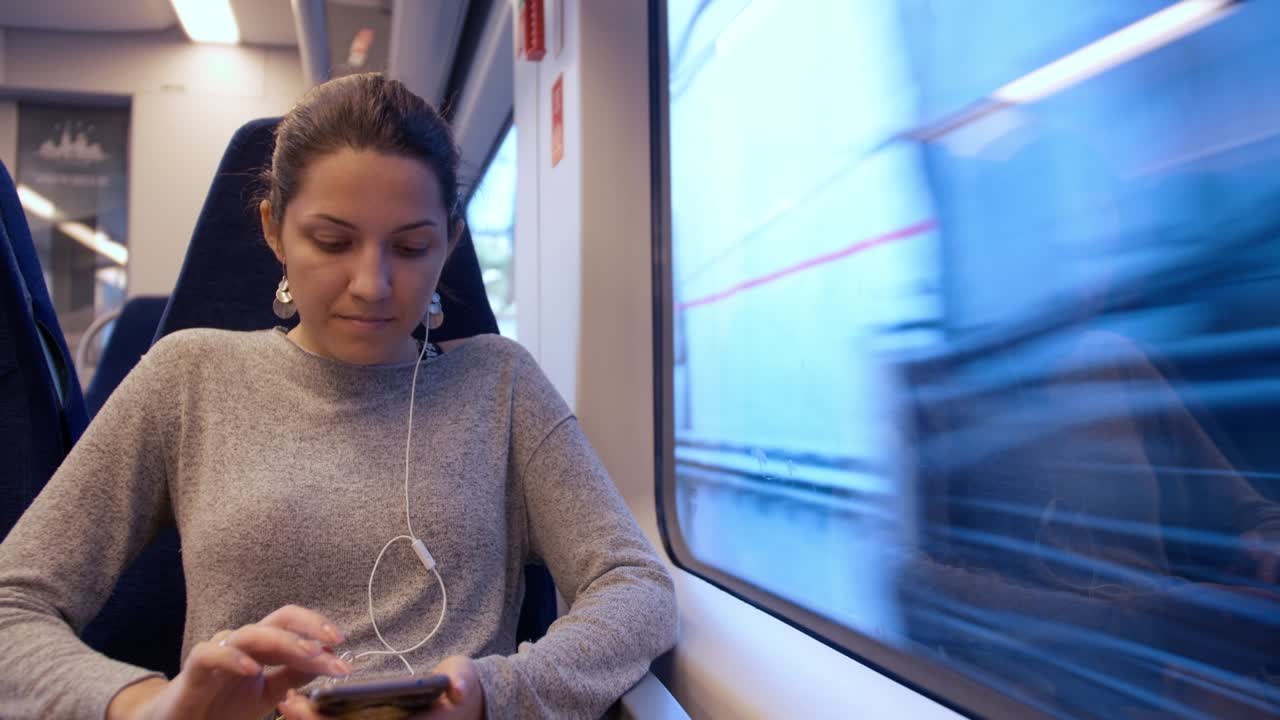 a young girl sits on a train by the window and uses a smartphone that is traveling in a tunnel