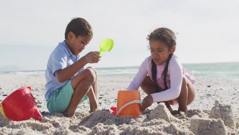 Happy-hispanic-brother-and-sister-playing-on-beach-with-sand-and-building-sand-castle