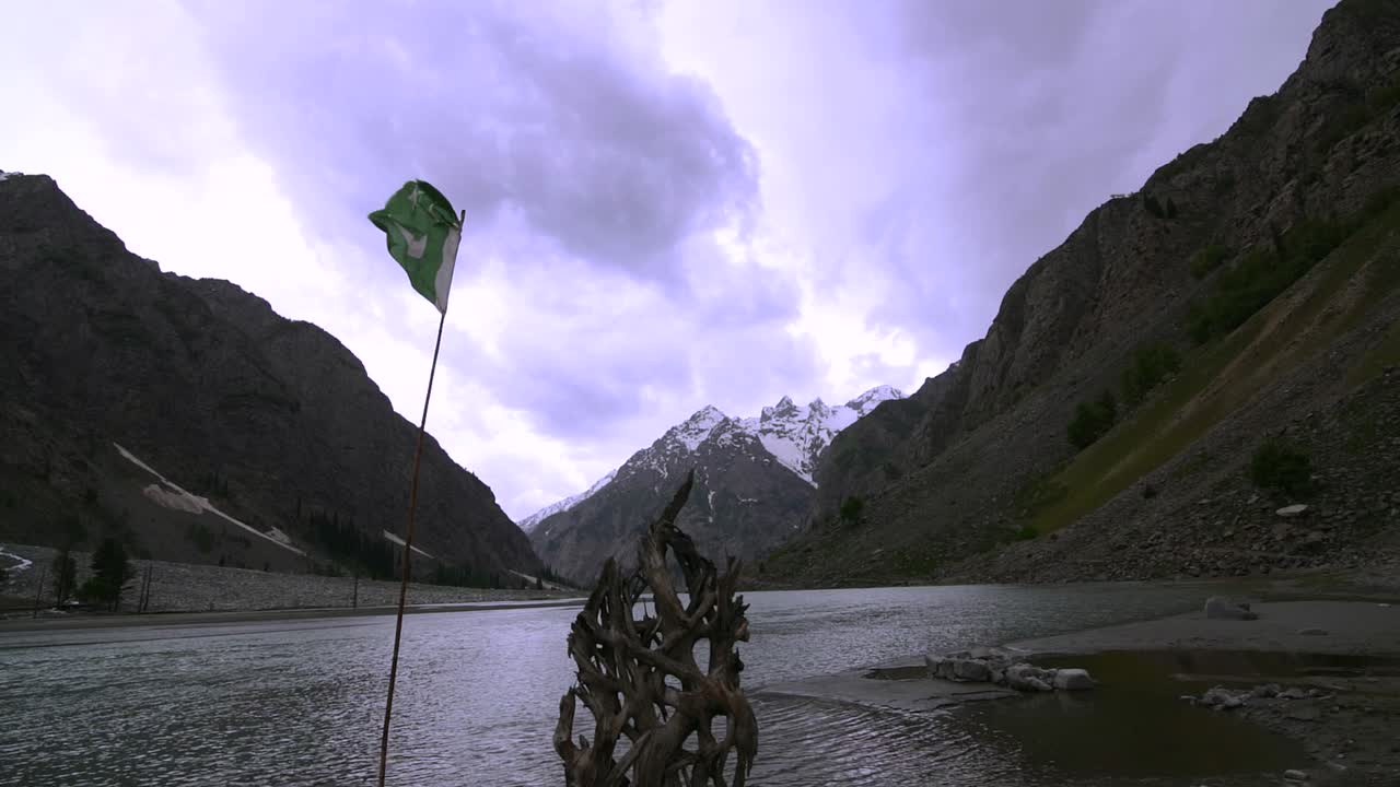 ondeando la bandera de pakistán en el medio de las montañas junto a un lago