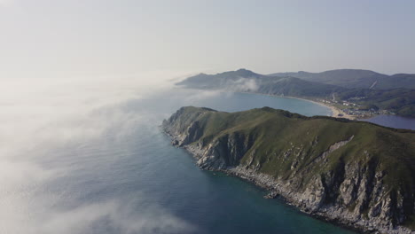 bird's eye view of a breathtaking steep rocky coast line with heavy dense fog approaching from the sea and moving over hill, far east, russia, sea of japan