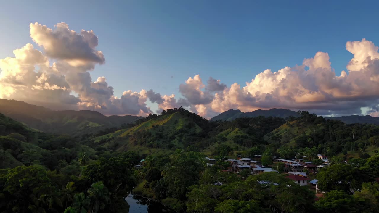 Aerial video view of a serene village nestled in lush green hills at sunset, capturing dramatic