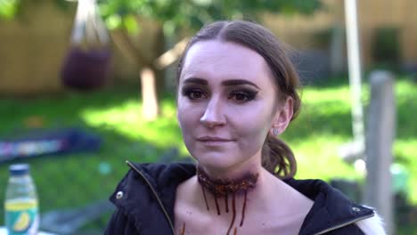 Horror-Make-up-Auf-Brünettem-Model,-Das-Draußen-Mit-Grünem-Hintergrund-Sitzt