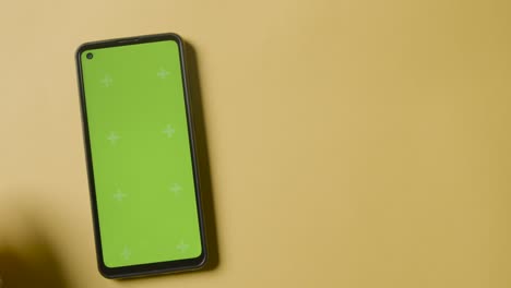 fotografía de estudio de una persona que usa un teléfono móvil de pantalla verde sobre un fondo amarillo 1