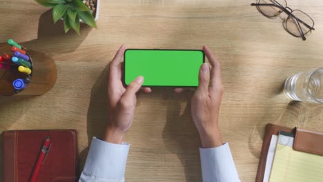 vista de arriba hacia abajo de una computadora portátil con pantalla verde simulada pantalla chromakey en un escritorio de oficina de madera al lado de la libreta con bolígrafos, gafas y un vaso de agua.