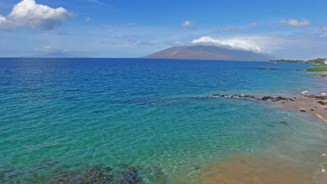 panning aerial shot over clear blue water in hawaii with land in background