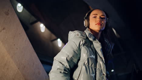 modelo de moda posando auriculares en la ciudad nocturna de cerca. mujer comiendo piruleta.