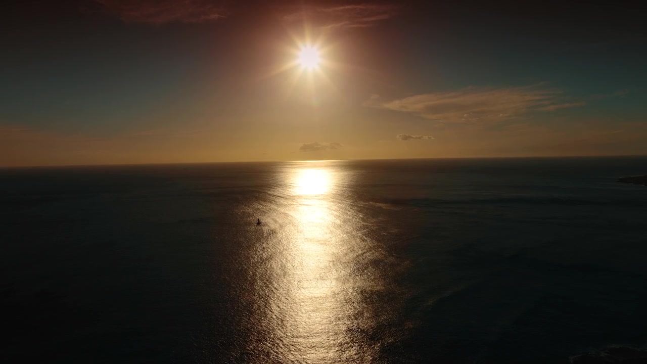 Setting sun above the dark waterscape of the peaceful ocean. Lonely person standing on the sup board rows with a paddle. Aerial view.