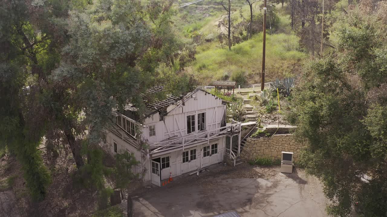 Aerial low descending shot of the damaged historic guesthouse at Will Rogers State Park after the Palisades Fire in Pacific Palisades, California. 4K