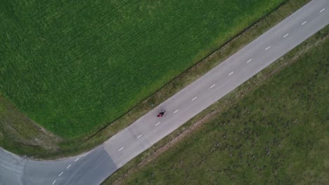 slowly turning aerial drone shot of motorcyclist driving down a road between grass field