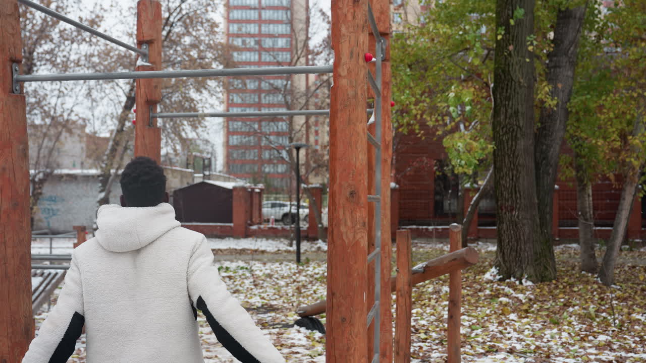 학생은 운동을 위해 따뜻해지고, 야외 운동 장비를 잡기 위해 점프하고, 풀업을 수행하고, 건물, 자동차 및 벌거벗은 나무가있는 도시 환경에서 즉시 떨어집니다.