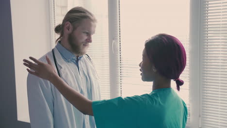 una linda y joven enfermera americana consuela a un joven médico con el pelo largo y rubio