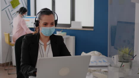 primer plano de una mujer de negocios con máscara facial usando auriculares hablando en el micrófono
