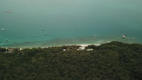 drone aéreo lento pan sobre isla tropical con agua azul clara con barcos