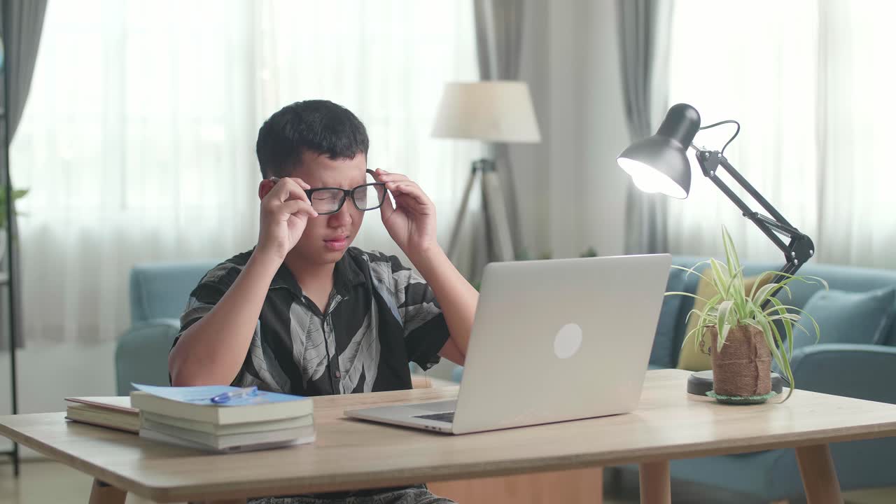 Remaja laki-laki belajar menggunakan laptop, mengalami mata lelah.