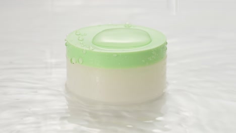 cosmetic product on water with splashes. beauty jar with cream on aqua background