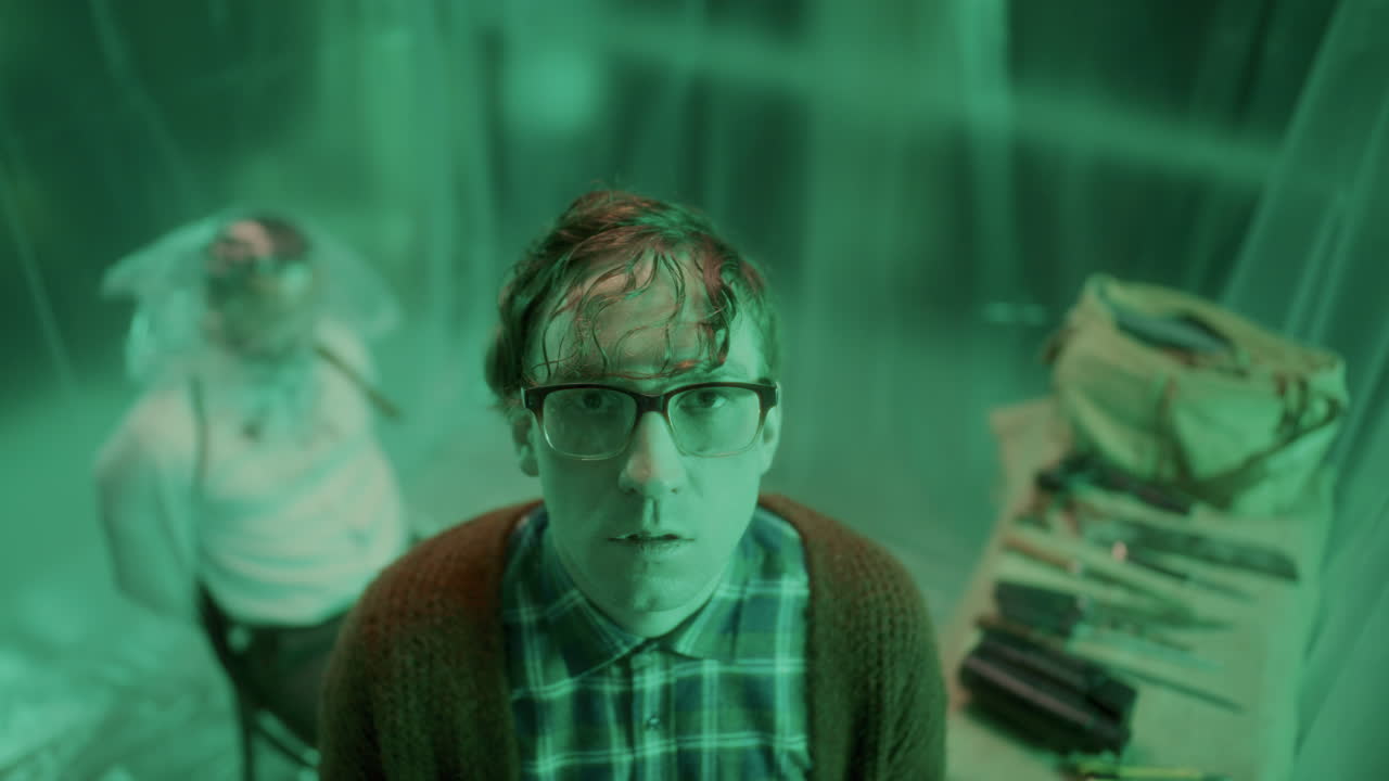 초록색으로 조명된 방에서 미치광이 연쇄 살인자의 초상화, 그의 뒤에 인 희생자와 함께