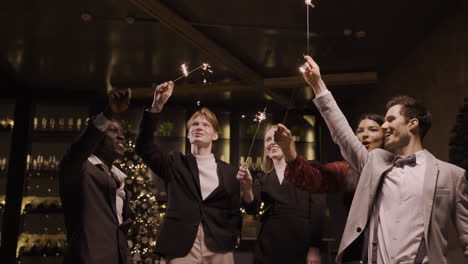 group of friends wearing stylish clothes and raising sparkles at new year's eve party