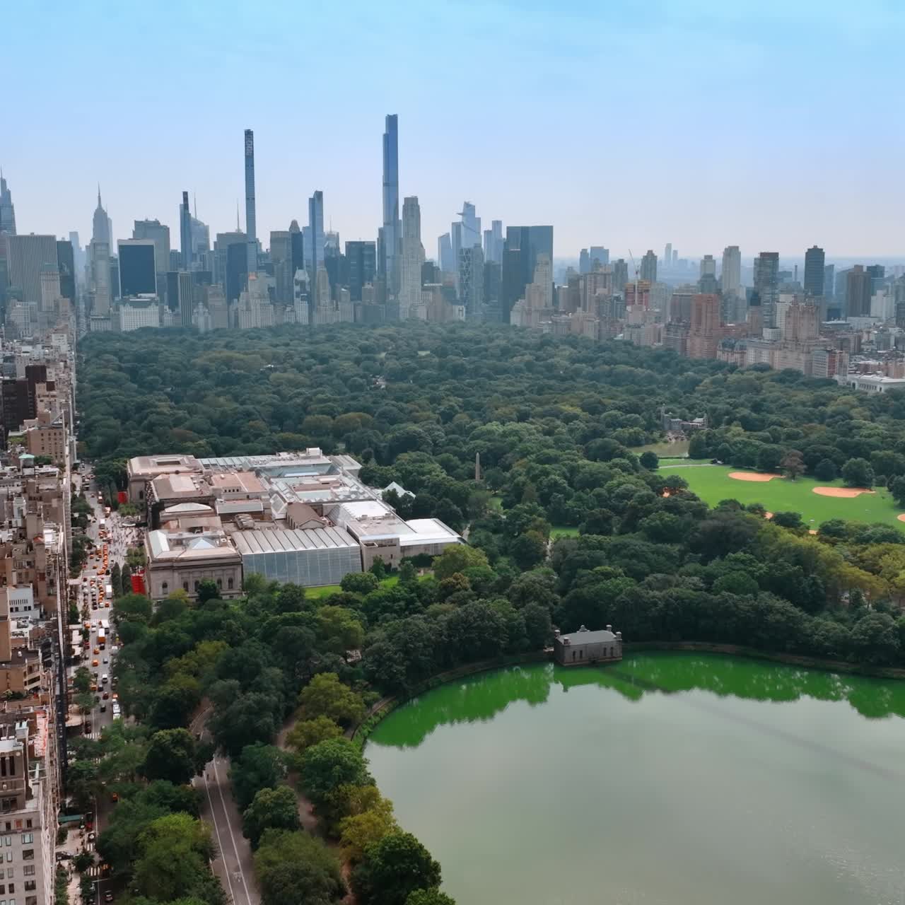 Lovely green area of Central Park in New York neighboring with dense city architecture. Beautiful sunny day footage above the metropolis. Skyscrapers at backdrop