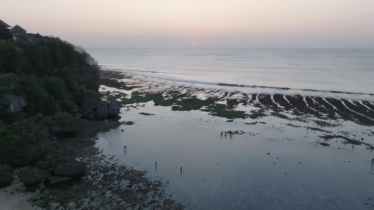 Synkende dronebilde over Bingin Beach lavvannsrev med solnedgang og menneskesilhuetter i Uluwatu, Bali, Indonesia