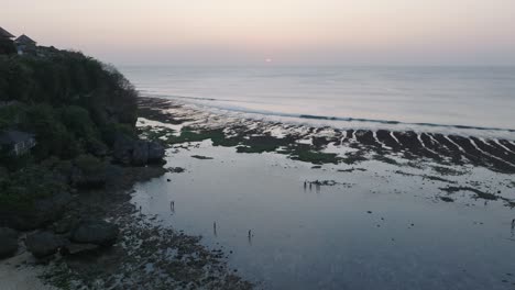 Drone-shot-descending-on-Bingin-Beach-low-tide-reef-with-sunset-and-human-silhouettes-in-Uluwatu-Bali-Indonesia