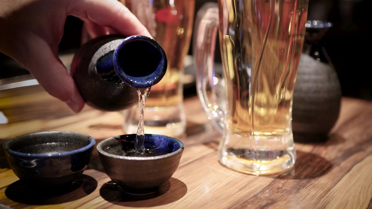 Tangan Menuangkan Sake Tradisional Jepang ke dalam Cangkir Keramik Kecil