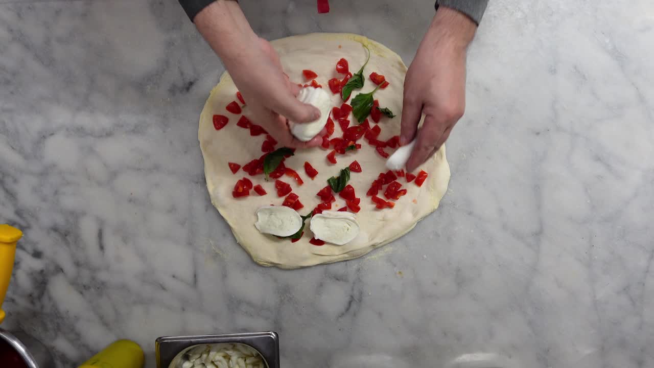 Vista dall'alto di uno chef italiano che condisce una pizza con pomodoro, mozzarella, basilico e olio d'oliva.