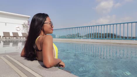 Mujer-Asiática-Parada-Al-Borde-De-Una-Piscina-Disfrutando-De-Un-Caluroso-Día-Soleado-En-Un-Lujoso-Hotel-Junto-A-La-Piscina-Durante-Sus-Vacaciones