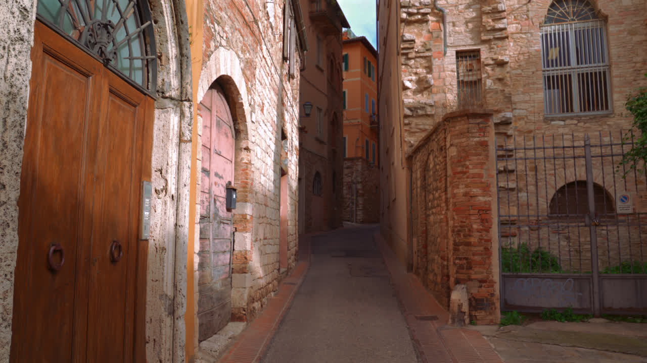 Antica strada ad arco con muri di mattoni e luce solare nel centro storico medievale di Perugia