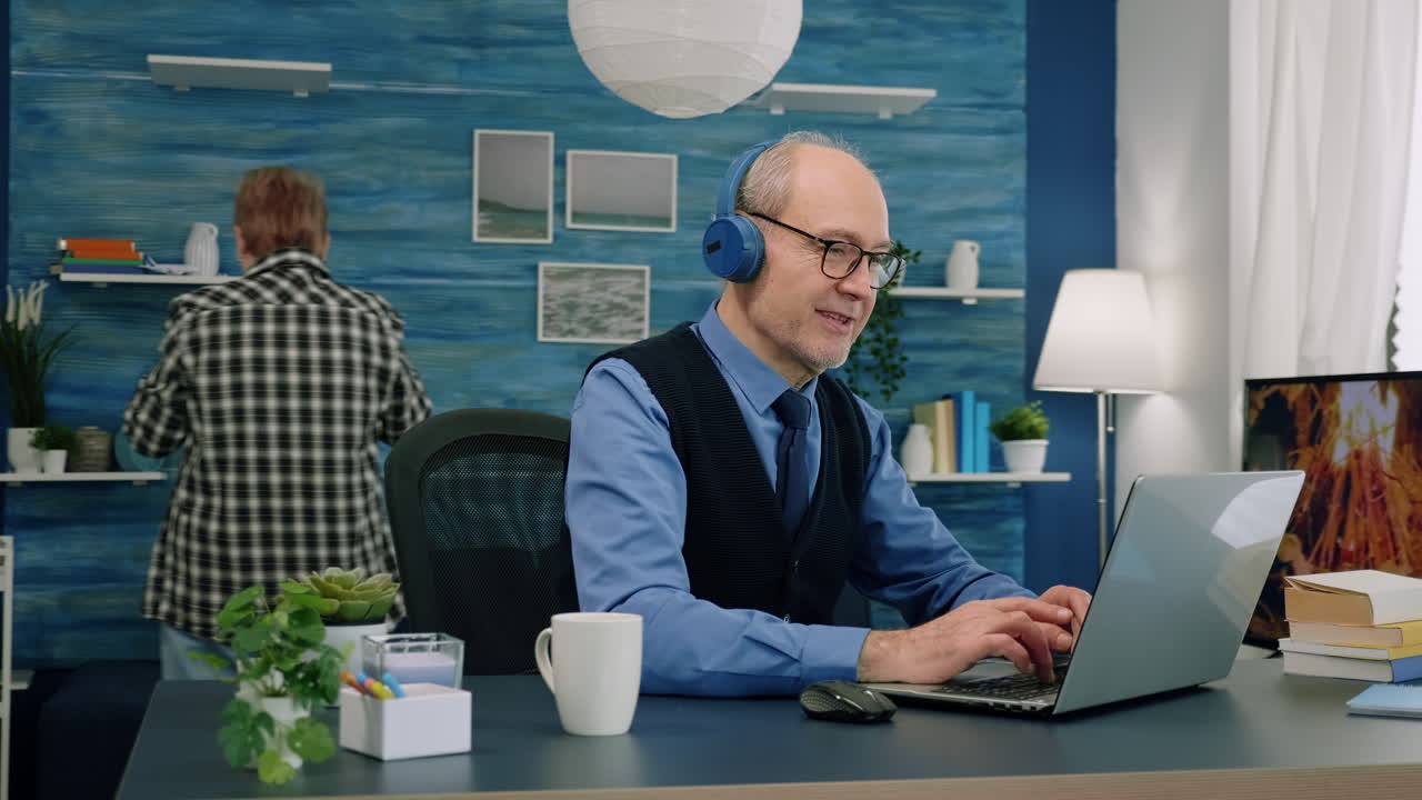 Senior old man listening music on headphones while working on laptop
