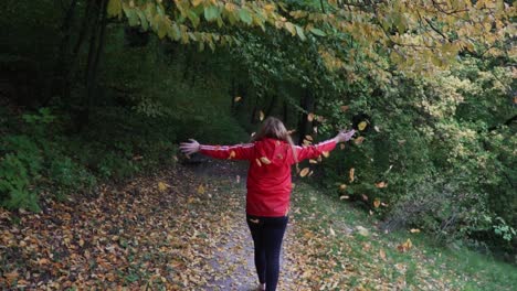 mujer con chaqueta roja caminando por el bosque alemán y tirando hojas al cielo por la emoción