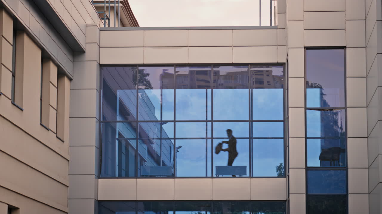 Silhouette professional walking across glass corridor highrise office building