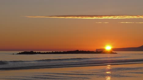 Sun-rising-over-headland-and-calm-shore,-gentle-ocean-waves,-mediterranean,-spain